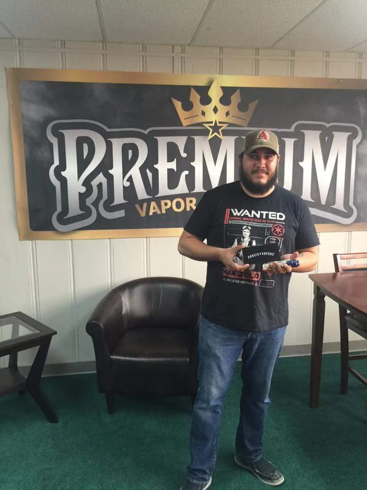 Premium Vapor Company staff member holding a new device in front of the store banner